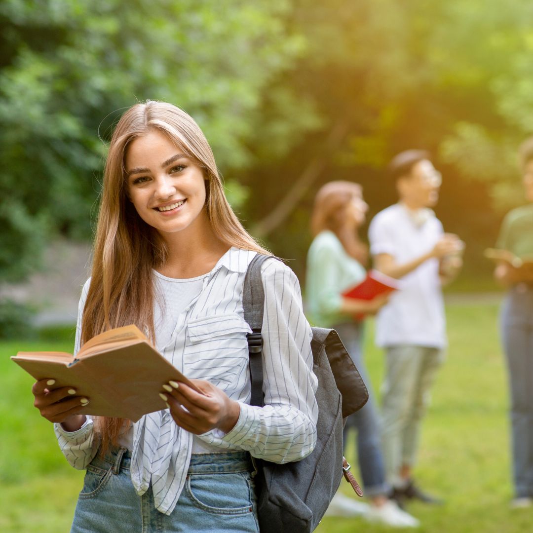 Degree Programs Abroad. Smiling Student With Book Posing Outdoor At Campus